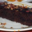 A dark, rectangular log of moist cake is spangled with toasted pecans, served on a plate decorated with cane syrup