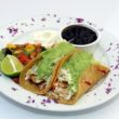 Fish tacos made with grilled mahi-mahi are dressed with cilantro-avocado sauce and sided by chunky papaya relish