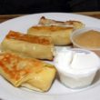 A plate of blintzes: griddle-cooked crepes wrapped around sweet pot cheese and accompanied by ramekins of sour cream and apple sauce