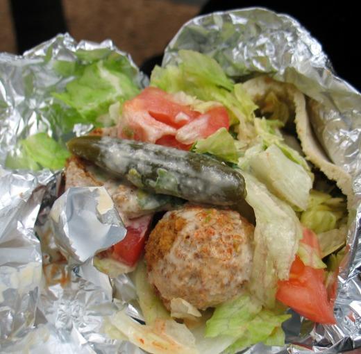 Street cart serves falafel wrapped in foil with tahini sauce and garnishes.