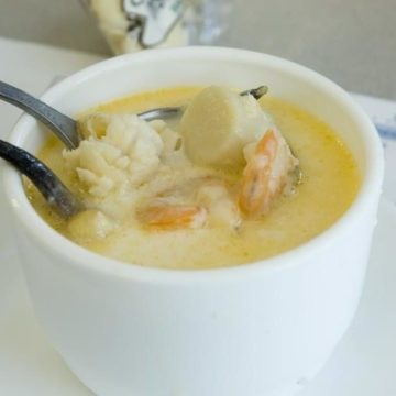 A bowl of cream-colored chowder is packed with scallops, shrimp, and flatfish