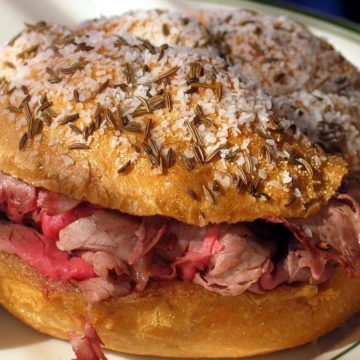 Thin-sliced roast beef is piled into a bun that is plastered with caraway seeds and coarse salt