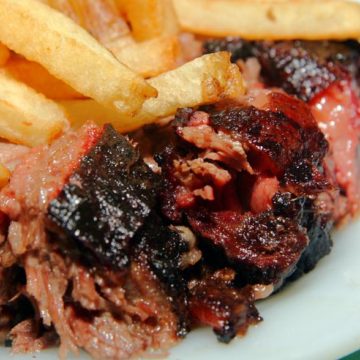 Chunks and shreds from the edges of BBQ brisket are piled up on a plate with French fries