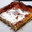 A thin square of gooey butter cake dusted with powdered sugar shows a chewy edge and custard-soft center