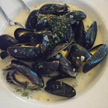 A bowl of steamed-open mussels in a pool of white wine and garlic