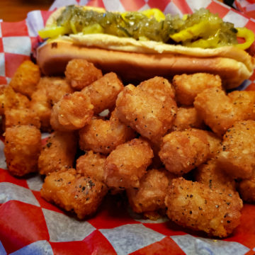 Crisp, golden-brown tater tots with a well-dressed hot dog in the background