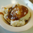 On a diner counter: a bowl holding a scoop of mashed potatoes covered with brown gravy