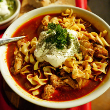 Bowl of chicken paprikash includes little dumplings and a crown of sour cream.