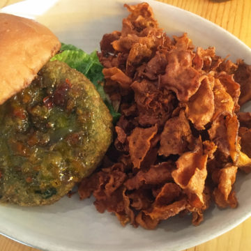 Green-hued burger made of falafel is dressed with red pepper jam and accompanied by sweet potato fries.