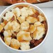 A cup of poutine is topped with gravy-drizzled cheese curds.