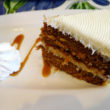 Elegant carrot cake plated with whipped cream and a caramel drizzle is topped with rich white cream cheese frosting
