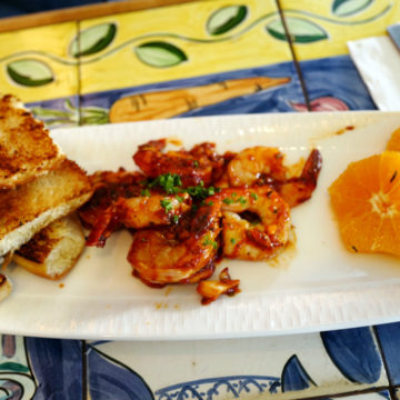 Prawns glazed with fire-roasted tomato sauce are accompanied on the plate by grilled focaccia and orange slices.