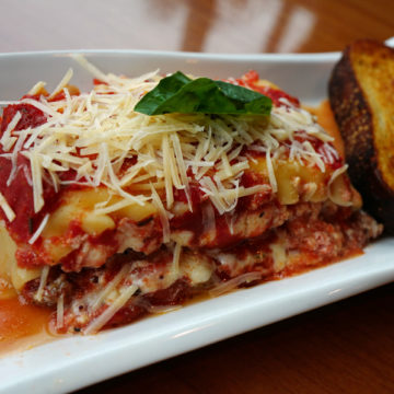 Broad, flat noodles are layered with cheese and sauce, accompanied by a slice of toasted Italian bread.