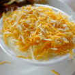 A bowl of hot grits is covered with shredded cheese about to melt