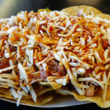 A broad field of tortilla chips is topped with BBQ pork, BBQ sauce, and cheese
