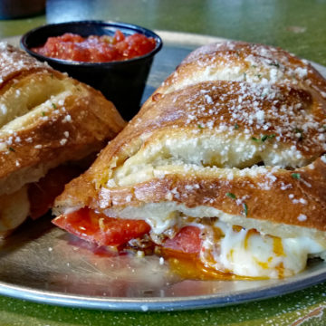 Rolled sandwich made of pizza crust dough is filled with mozzarella, pepperoni, and sausage, accmopanied by red sauce