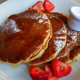 A stack of dark gold pancakes with fresh strawberries, butter, and maple syrup
