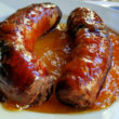 A pair of crisp-skinned pork sausages on a puddle of orange-apricot jam