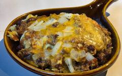 Ceramic pan holds a hamburger topped with eggs, chili, hash browns, cheese, and onions