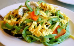 Barley green hand-shaven noodles are arrayed on a plate with chicken and vegetables.