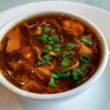 A bowl of hot & sour soup glows red with pepper flavor.