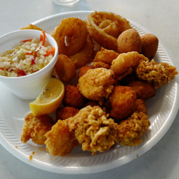 A fried seafood platter of oysters, scallops, shrimp, onion rings, and hushpuppies, plus a cup of cole slaw