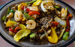 Sizzling fajita platter includes beef, chicken, and shrimp, plus vegetables.