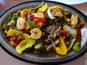 Sizzling fajita platter includes beef, chicken, and shrimp, plus vegetables.