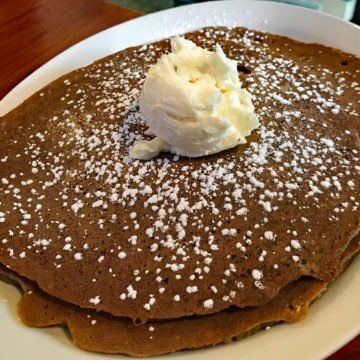 Stack of thin, plate-wide gingerbread pancakes is topped with a globe of butter.