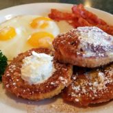 Cinnamon roll, sliced horizontally into three rounds, is fried golden brown like French toast, sided by three eggs and bacon