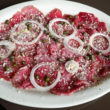 Plate of thin-sliced raw beef adorned with onions, herbs, and a sprinkle of hard cheese