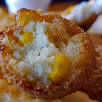 Cross-section of a crisp-fried spherical hushpuppy showes the inside dotted with corn kernels