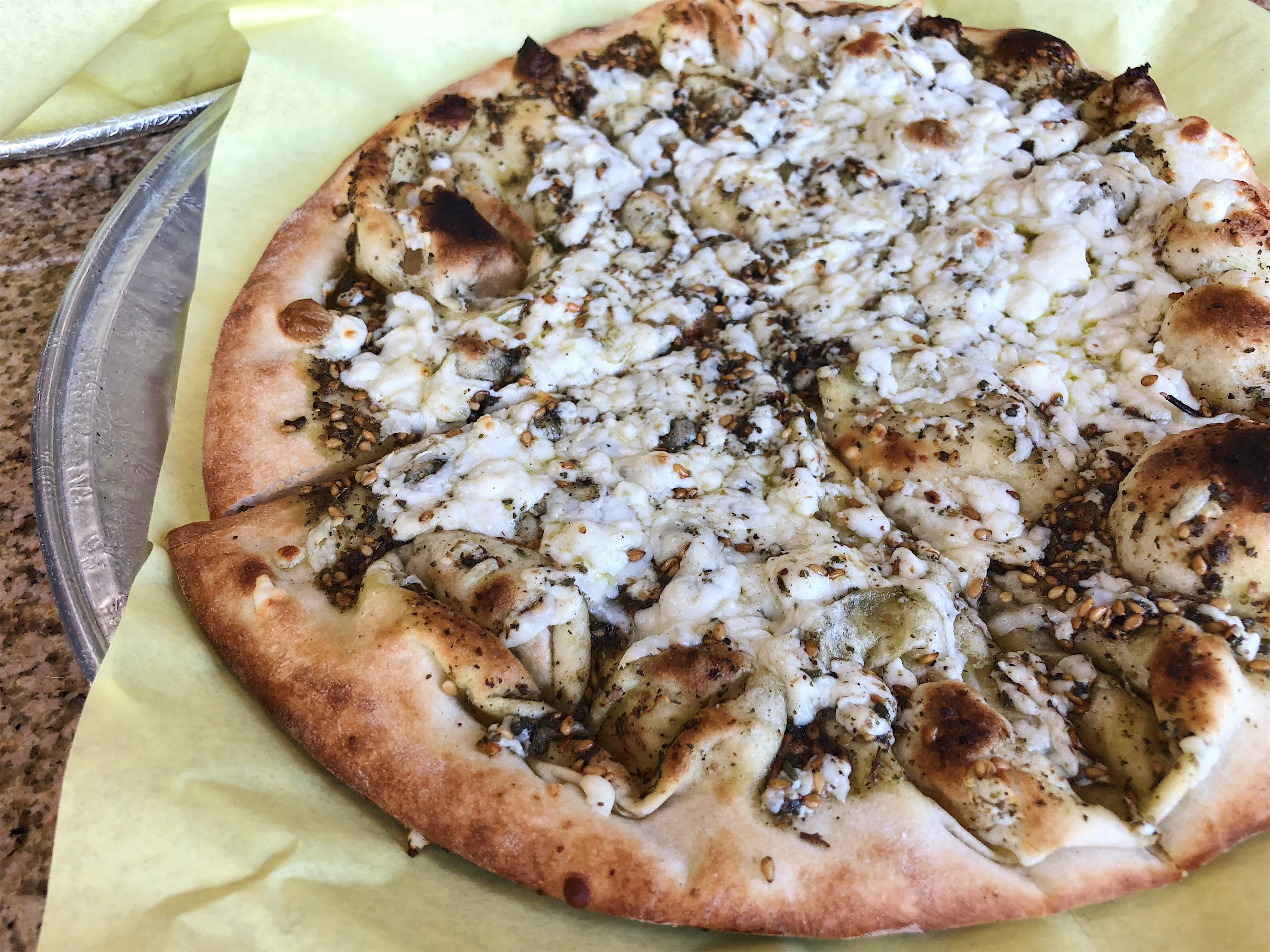 Flatbread topped with melted feta cheese and dark spices at Al Amir Bakery