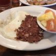 Corned beef and eggs on a diner plate, accompanied by a bowl of fruit