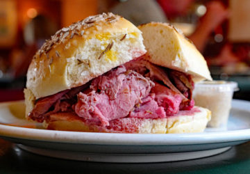 Thin-sliced rare roast beef is piled into a roll spangled with coarse salt and caraway seeds