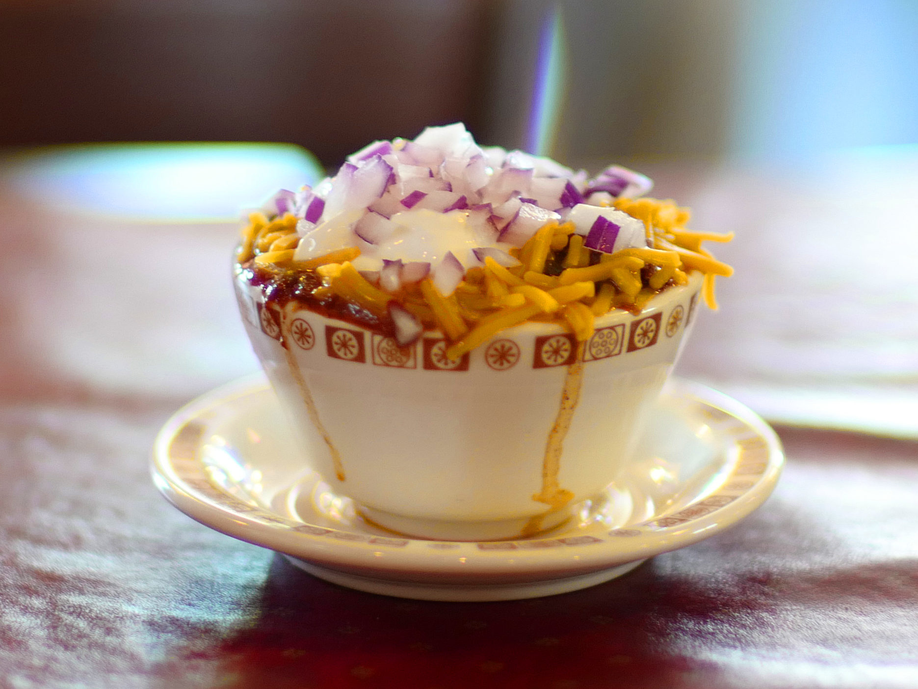 Cup of chili topped with cheese and chopped raw onions