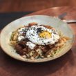 Kimchi hash, full of vegetables, is topped with a fried egg and herbs.