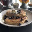 A plate of hefty sourdough pancakes is topped with whipped butter and sauteed blueberries