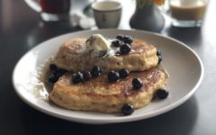 A plate of hefty sourdough pancakes is topped with whipped butter and sauteed blueberries