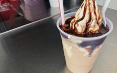 In a plastic cup, a chocolate milk shake is topped with hot fudge and more ice cream