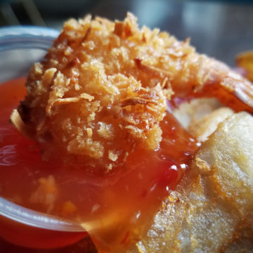 A crunchy coconut shrimp is being dipped in sweet-hot chili sauce.