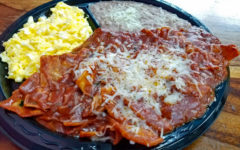 Broad partitioned plate holds tortilla chips topped with chile and cheese, plus scrambled eggs and refried beans.