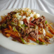 A plate of French fries piled with bacon, beef, cheese, shrimp, and veggies