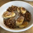 A bowl holds dark chia pudding topped with spiced puffed rice and slices of caramelized banana