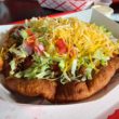 Puffy, plate-size fry bread holds ground beef, lettuce, tomato, and shredded cheese.
