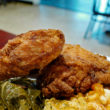 Fried chicken drumstick and thigh rest upon greens and corn
