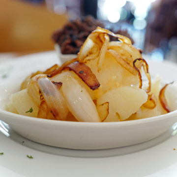 Bowl of soft-cooked pieces of yucca draped with sizzled onions