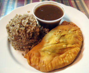 A mound of "dirty rice" and cup of gravy accompany a pastry crescent filled with beef and pork sausage