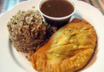 A mound of "dirty rice" and cup of gravy accompany a pastry crescent filled with beef and pork sausage