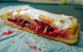 Slice of cherry strudel is topped with white sugar icing.